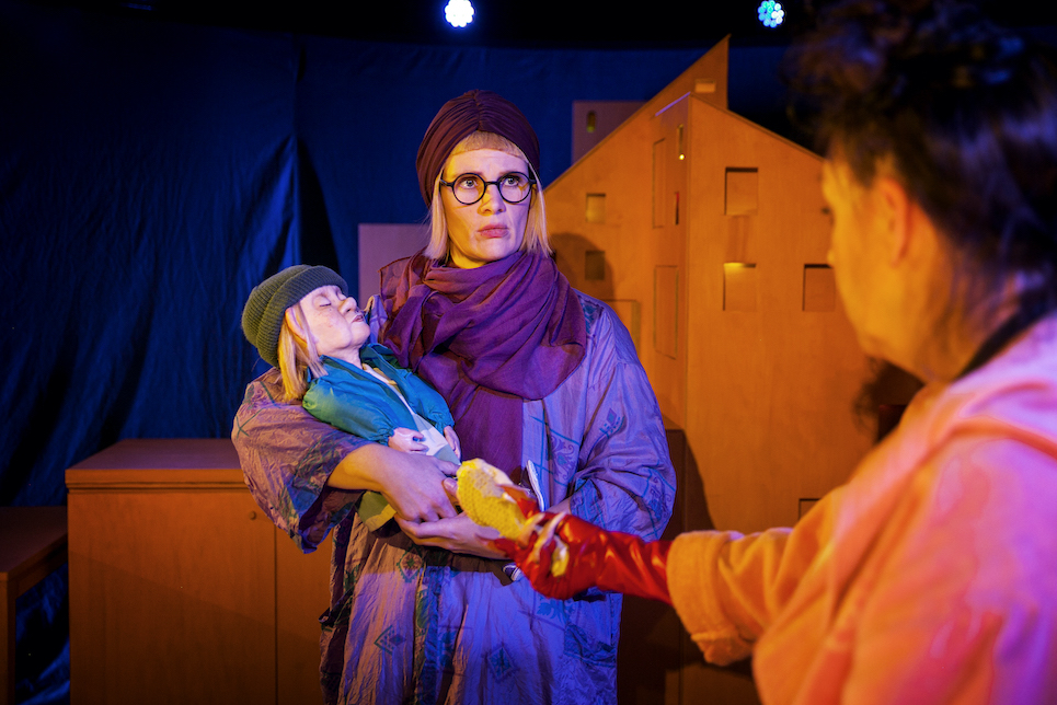 Foto på Mormor (som spelas av samma skådespelare som Åke) som håller i en docka som föreställer Åke. I förgrunden är Mamma som försöker ge Mormor en smält glass.